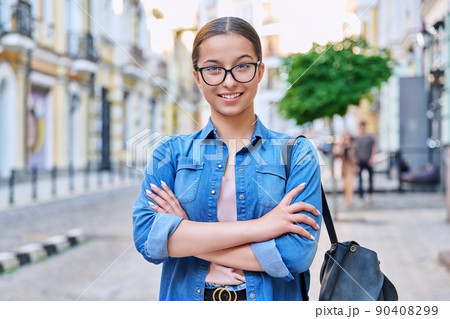 Confident teenage girl in glasses with backpack looking at camera outdoor 90408299