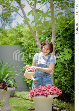 An Asian woman is watering plants in the garden. An Asian woman is watering plants in the garden. 90410649