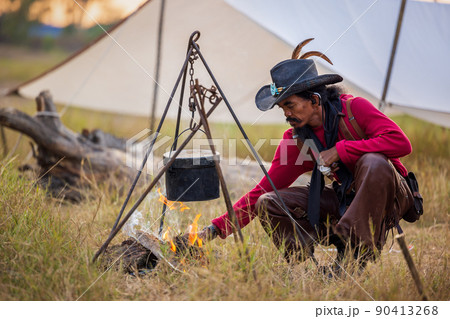 Traveling avenger style, the cowboys have outside camping, heating hot water, In a campsite, a cast iron pot cooks over an open fire. Traveling avenger style, the cowboys have outside camping, heating hot water, In a campsite, a cast iron pot cooks over an open fire. 90413268