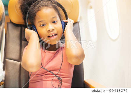 Girls peering out the plane's window. During a holiday flight, a child looks out the window, joyful. Girls peering out the plane's window. During a holiday flight, a child looks out the window, joyful. 90413272