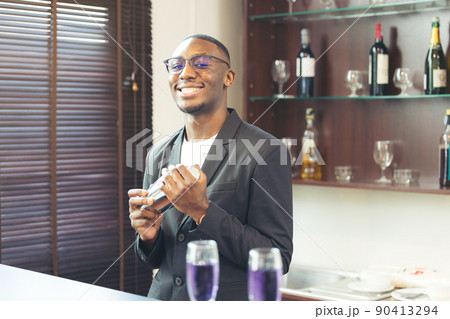 Making a beverage, a black handsome bartender smiles at the camera. Making a beverage, a black handsome bartender smiles at the camera. 90413294