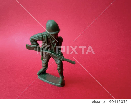 敵へ向かって銃を構える兵士の人形（赤背景）、戦争イメージ 90415052