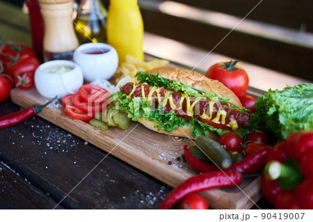 BBQ hot dog served with vegetables and French fries and sauces on wooden serving board 90419007