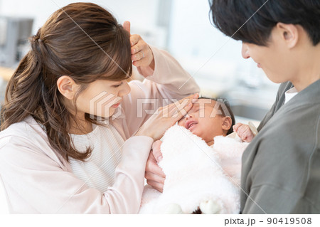泣いている赤ちゃんのおでこに手を当てて熱を測る若いママとパパ 泣いている赤ちゃんのおでこに手を当てて熱を測る若いママとパパ 90419508