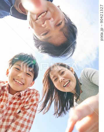 青空のもと笑顔でカメラを覗き込む3人家族 90421327
