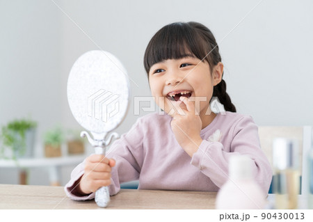 鏡で抜けた歯を見る小学生の女の子 90430013