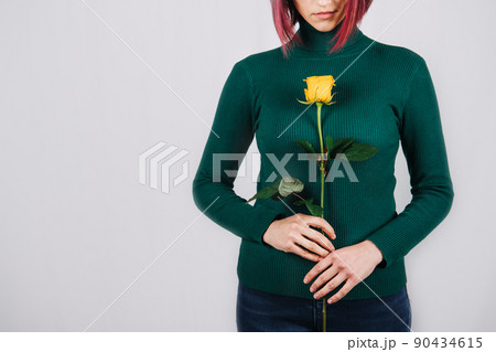 Faceless portrait of woman with yellow flower in hand near breast on light background. Faceless portrait of woman with yellow flower in hand near breast on light background. 90434615