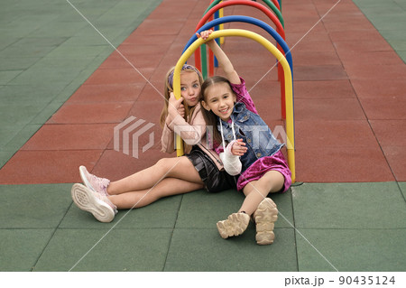 Joy little preschool girl with broken arm and cast on her forearm having fun at children's sports playground with her friend despite the injury. Best friends forever. Accident insurance 90435124