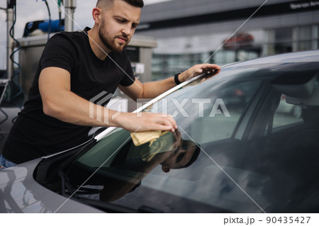 Man wipes a windshield of his car with a rag in a showroom at a self-service car wash Man wipes a windshield of his car with a rag in a showroom at a self-service car wash 90435427