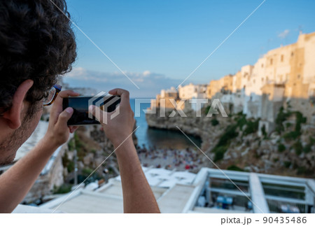 Polignano a mare, Puglia, Italy. August 2021. A young man with curly hair and glasses admires the view of Cala Monachile 90435486