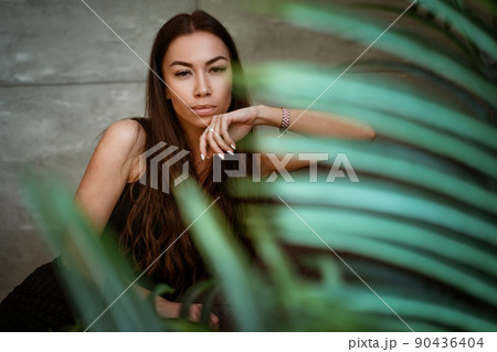 Woman portrait on a background of a gray wall through the leaves of a flower Woman portrait on a background of a gray wall through the leaves of a flower 90436404