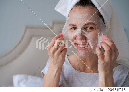 Nice woman with towel on her head applies moisturizing mask to her face Nice woman with towel on her head applies moisturizing mask to her face 90436713
