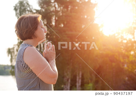 Peaceful woman holds her palms in front her in prayer against backdrop trees 90437197