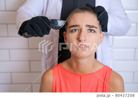 Young woman is forcibly shaving her head with an electric razor, holding 90437208