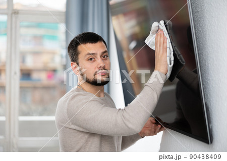 Man wipes a tv in a living room with rag Man wipes a tv in a living room with rag 90438409
