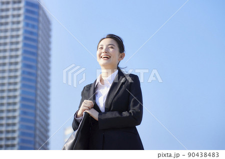 リクルートスーツの若い女性　青空　高層ビル　笑顔 90438483