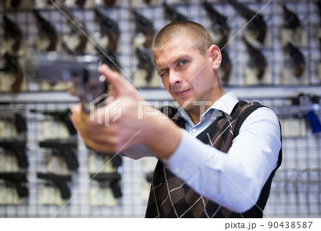 Focused man testing pistol aiming in armory shop 90438587