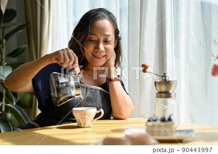 Cheerful Asian aged-woman brewing her morning coffee in the house Cheerful Asian aged-woman brewing her morning coffee in the house 90443997