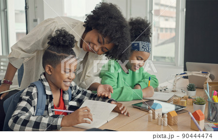 Classroom with diverse learners of happily African American students and teacher doing activities together. The teacher is teaching, guiding and talking to the children in diverse. 90444474