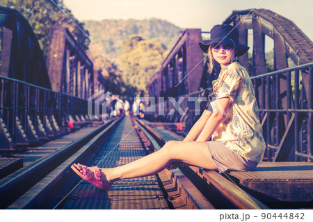 Female Asian tourist is sitting on the old train track of River Kwai Historical site in Kanchanaburi, Thailand. 90444842