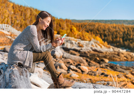 Mobile phone travel lifestyle Asian woman using cellphone data durig outdoor hiking adventure in Quebec, Canada. Happy girl texting in forest autumn foliage. Technology 90447284