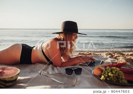 Young Woman Dressed in Swimsuit Working on Laptop During Picnic by the Sea 90447603