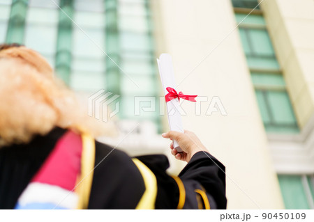 Happy Asian graduate student holding the diplomas on hand during the university graduation ceremony. Master degree student in gown suit holding a diplomas for photography. Happy Asian graduate student holding the diplomas on hand during the university graduation ceremony. Master degree student in gown suit holding a diplomas for photography. 90450109