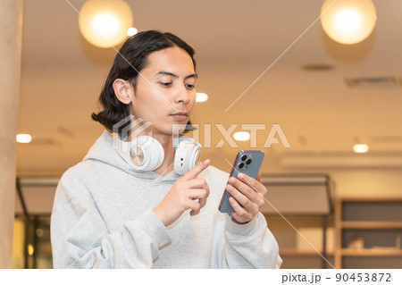 スマホを持つヘッドフォンの男性 90453872