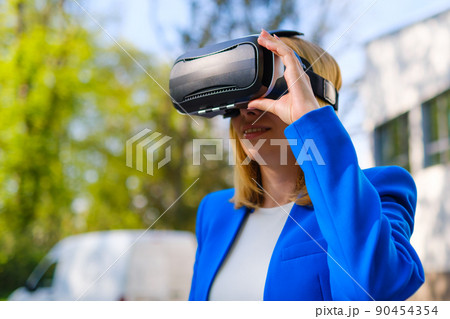 Woman with VR virtual reality goggles experiences a metaverse world. Augmented reality technology concept Woman with VR virtual reality goggles experiences a metaverse world. Augmented reality technology concept 90454354