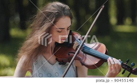 A young girl plays the violin in the city park. 90455140
