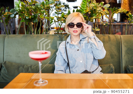 Portrait of attractive young woman drinking coctail in cafe indoor. Beautiful blonde woman relaxing at the bar and drinking a cocktail Portrait of attractive young woman drinking coctail in cafe indoor. Beautiful blonde woman relaxing at the bar and drinking a cocktail 90455271