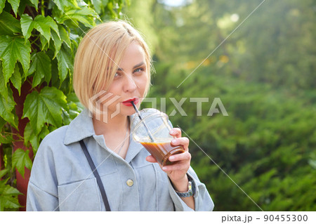 Stylish young blonde walks around the city and drinks a cold drink. Stylish young blonde walks around the city and drinks a cold drink. 90455300
