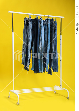 Rack with different jeans on yellow background 90456542