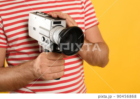 Man with vintage video camera on yellow background, closeup Man with vintage video camera on yellow background, closeup 90456868