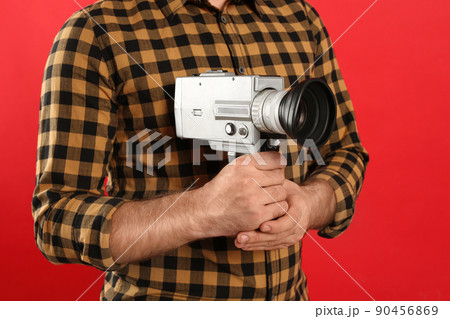 Young man with vintage video camera on red background, closeup Young man with vintage video camera on red background, closeup 90456869