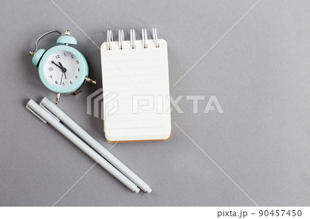 Top view of blank note paper with pen and alarm clock on gray background 90457450