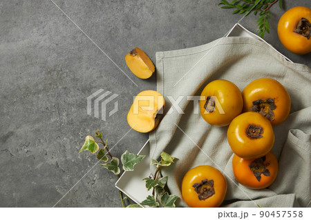 Top view of a light blue napkin of persimmon , green leaf in grey background for food advertising  90457558