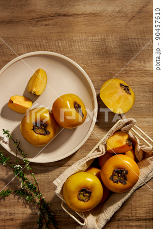 Top view of persimmon in white plate , flower , green leaf with grey background and blank space for advertising Top view of persimmon in white plate , flower , green leaf with grey background and blank space for advertising 90457610