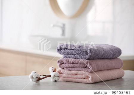 Stack of fresh towels and cotton flowers on table in bathroom 90458462