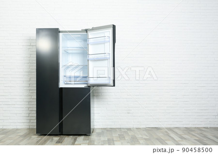 Modern empty refrigerator near white brick wall, space for text 90458500