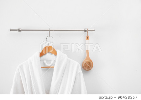 Hanger with clean bathrobe and brush on light wall 90458557