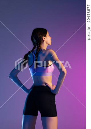 Back view. Young fitness girl, female athlete in sports uniform posing isolated on pink blue background in neon. Sport, track-and-field athletics, competition concept 90458677