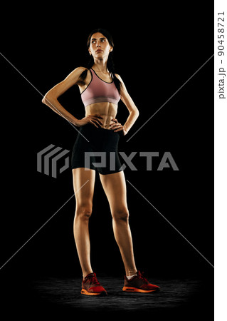 Portrait of young girl, female athlete in sports uniform posing isolated on black studio background. Sport, track-and-field athletics, competition concept 90458721