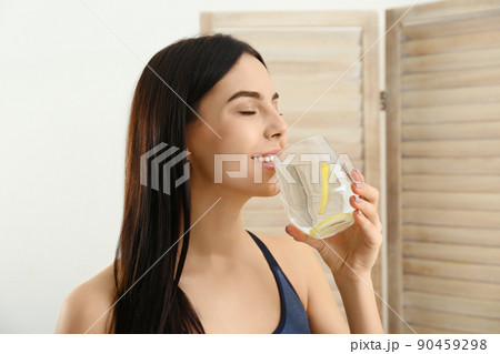 Beautiful sportive woman drinking fresh lemon water indoors Beautiful sportive woman drinking fresh lemon water indoors 90459298