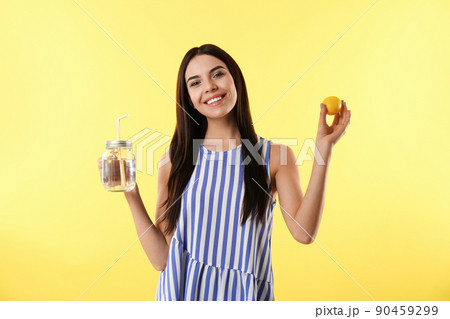 Beautiful young woman with tasty lemon water and fresh fruit on yellow background Beautiful young woman with tasty lemon water and fresh fruit on yellow background 90459299