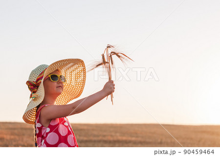 Child girl in straw hat dress in wheat field. Smiling kid in sunglasses sunset countryside. Cottagecore style aesthetic. 90459464