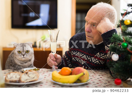 Lonely elderly man feeding cat at table during celebration of New Year Lonely elderly man feeding cat at table during celebration of New Year 90462233