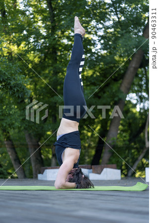 Athletic young woman stands on her head. Girl practices yoga in the pose of Shirshasana. 90463311