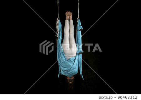 Young girl gymnast in sportswear doing stretching while hanging upside down. Aero fly yoga. Isolated on black background. 90463312