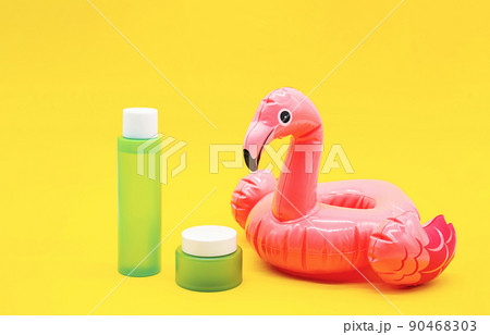 Set of green cosmetic bottle, jar and inflatable pink flamingo on yellow background. Summer collection of skin care product. Set of green cosmetic bottle, jar and inflatable pink flamingo on yellow background. Summer collection of skin care product. 90468303